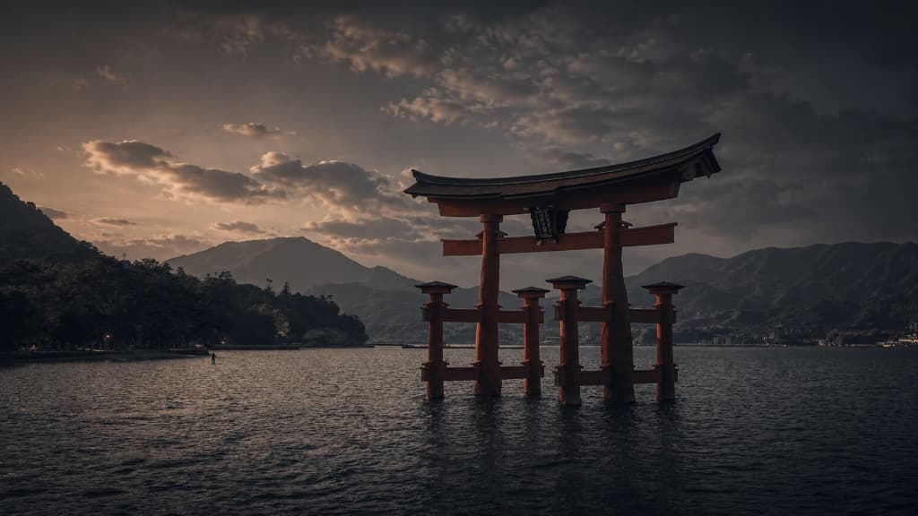 Itsukushima Shrine floating Torii gate on calm water at golden sunset with mountain backdrop