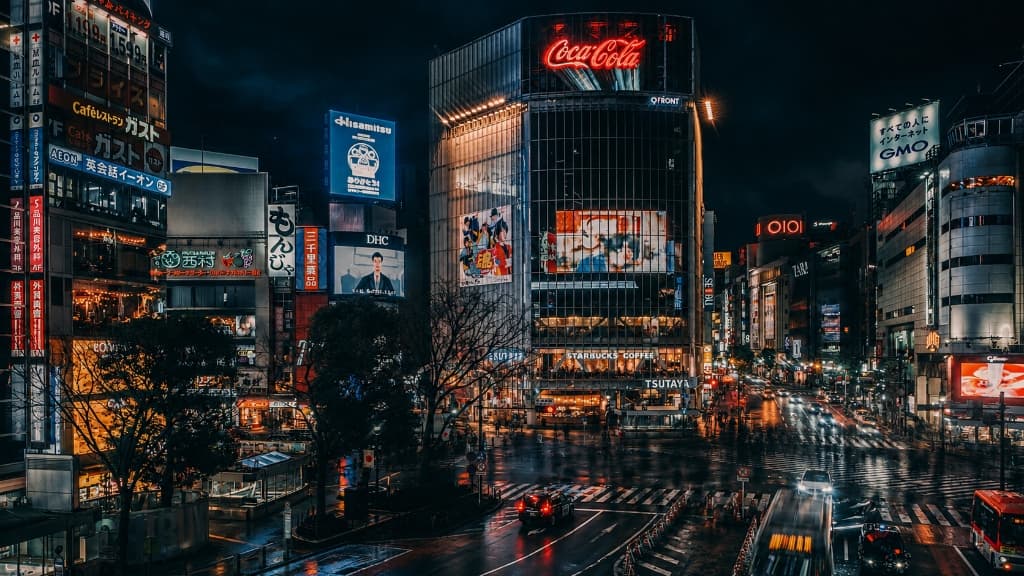 Tokyo Shibuya Crossing at night with QFRONT building, digital billboard screens, and connected city traffic